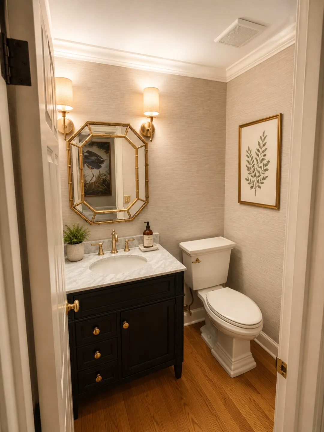 Powder room renovation with black vanity, gold mirror, and grasscloth wallpaper