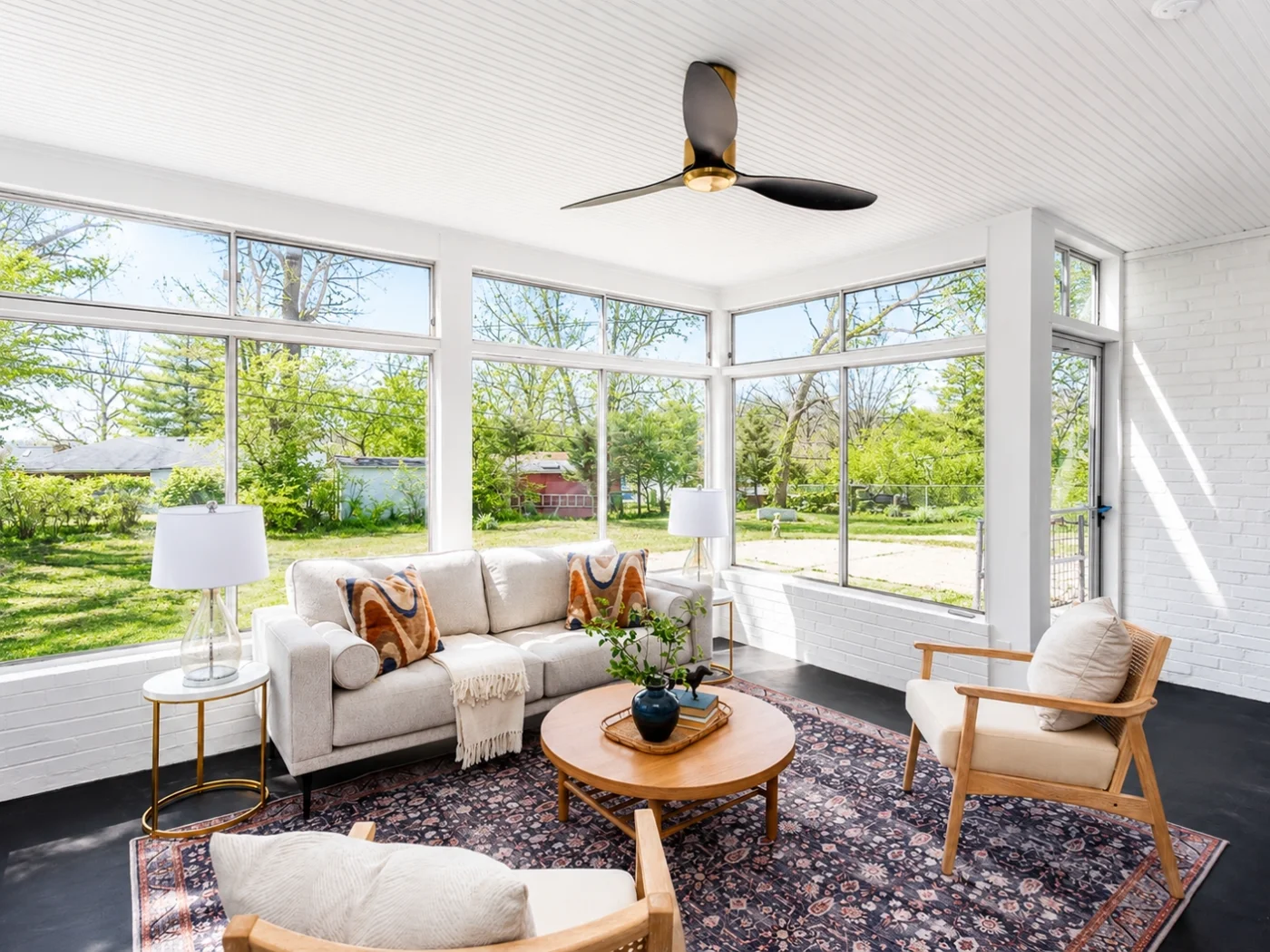 Bright sunroom with floor-to-ceiling windows, painted white brick, and mid-century modern furniture